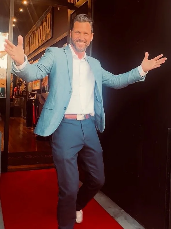 Gregory smiling with open arms on the gallery red carpet