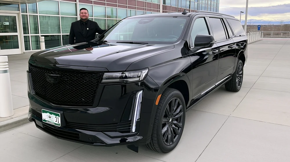 Black Cadillac Escalade and chauffeur outside a glass terminal building