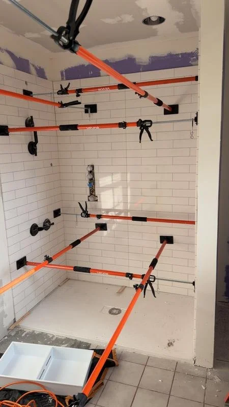 Shower wall panels held by bracing clamps while the adhesive cures