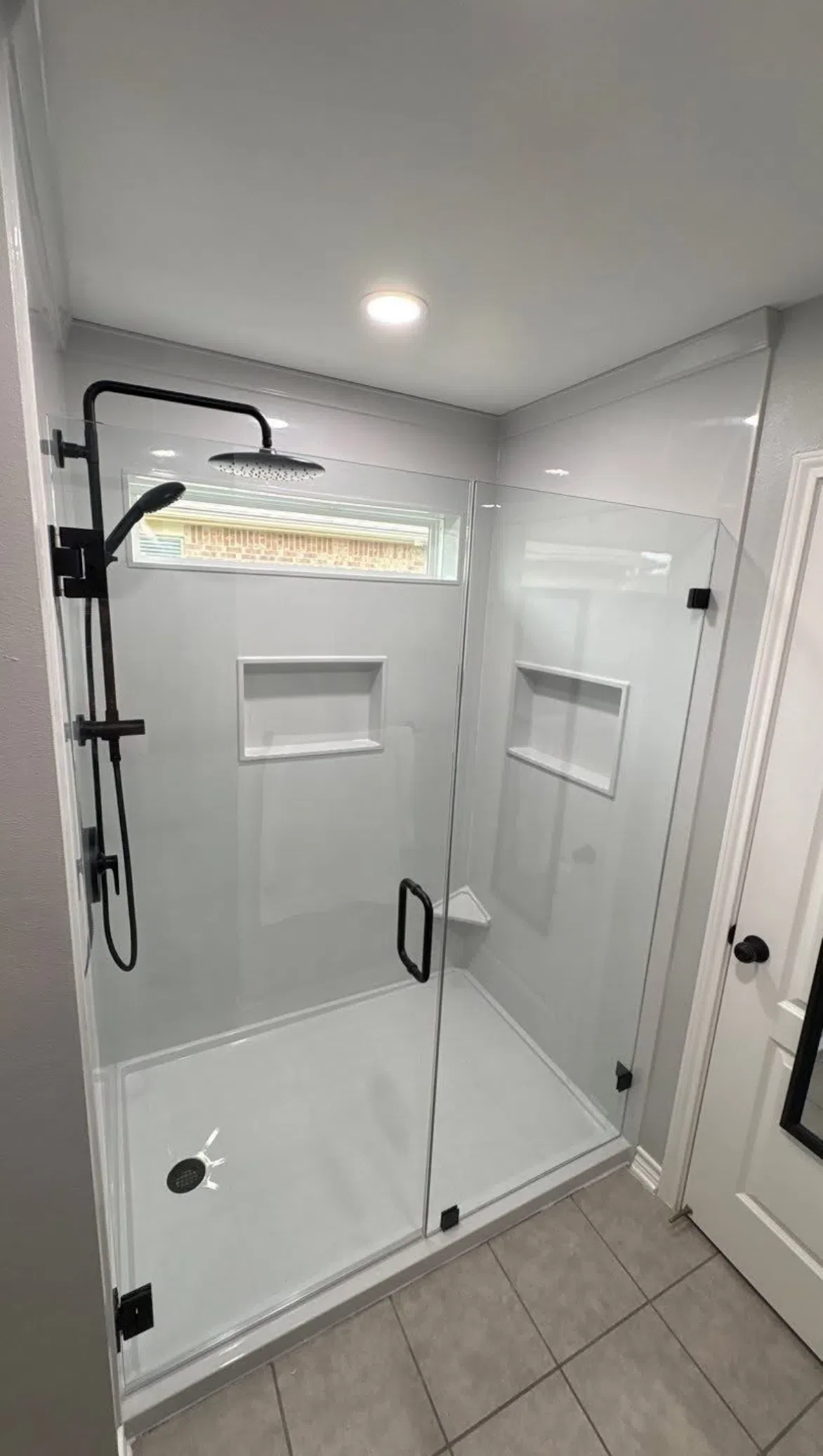 Walk-in shower with matte black fixtures, rainfall showerhead, and recessed shelf