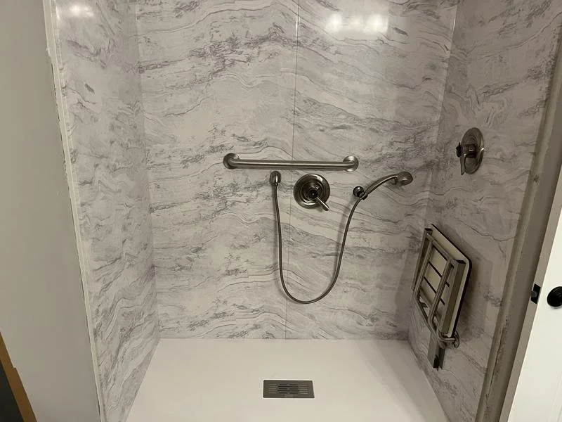 Marble-look panel walk-in shower with structural grab bars, a handheld showerhead, and a fold-down seat