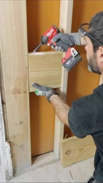 Open bathroom wall during a grab bar installation showing solid wood blocking installed between the studs