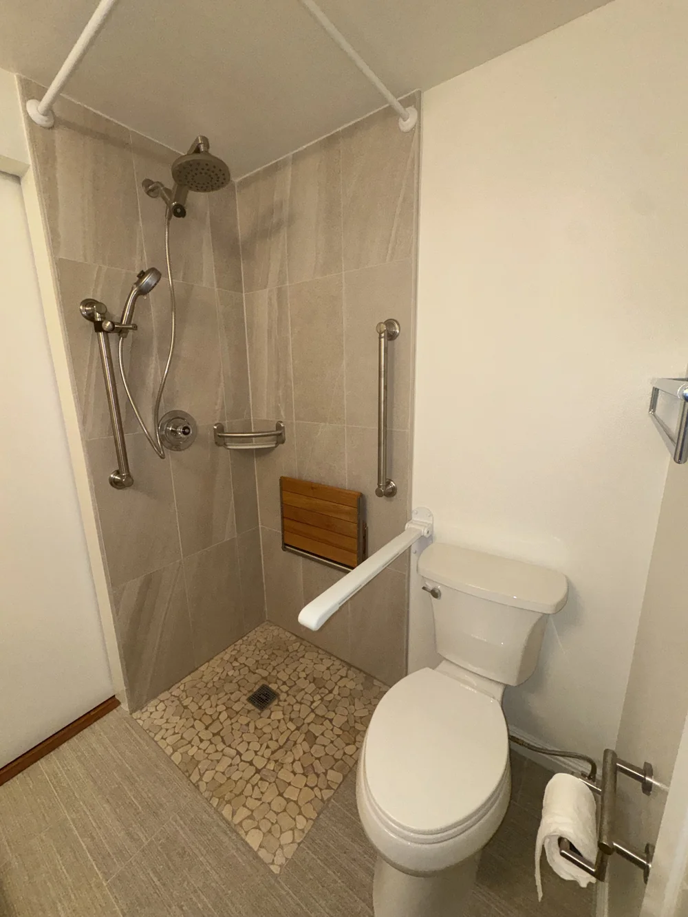 Completed zero-threshold walk-in shower with fold-down teak bench, grab bars, and handheld showerhead