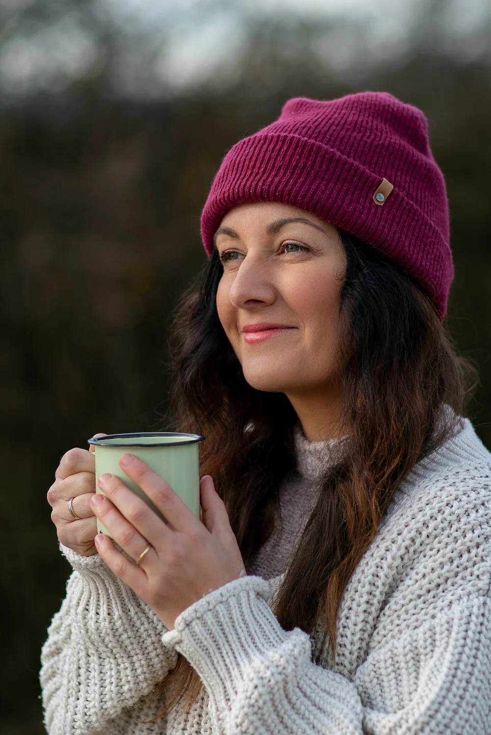Lachende Frau mit Beanie und Tasse im Wald
