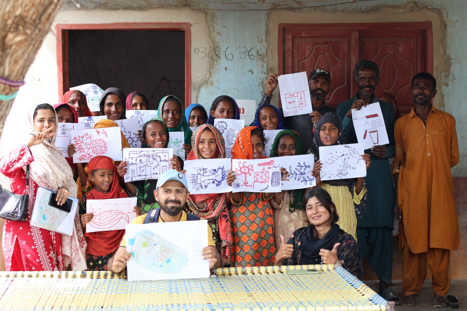 Children and neighbors in Sindh, Pakistan, hold up drawings of what they want to build
