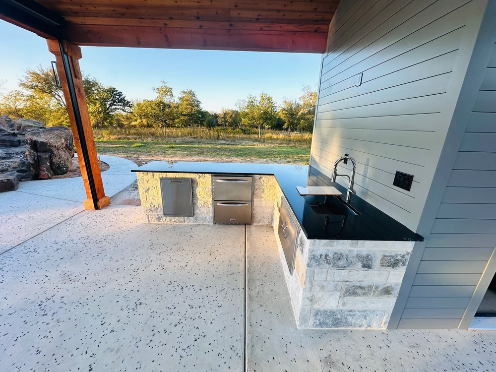Munday stone outdoor kitchen with sink, dark countertop and stainless storage in Burleson