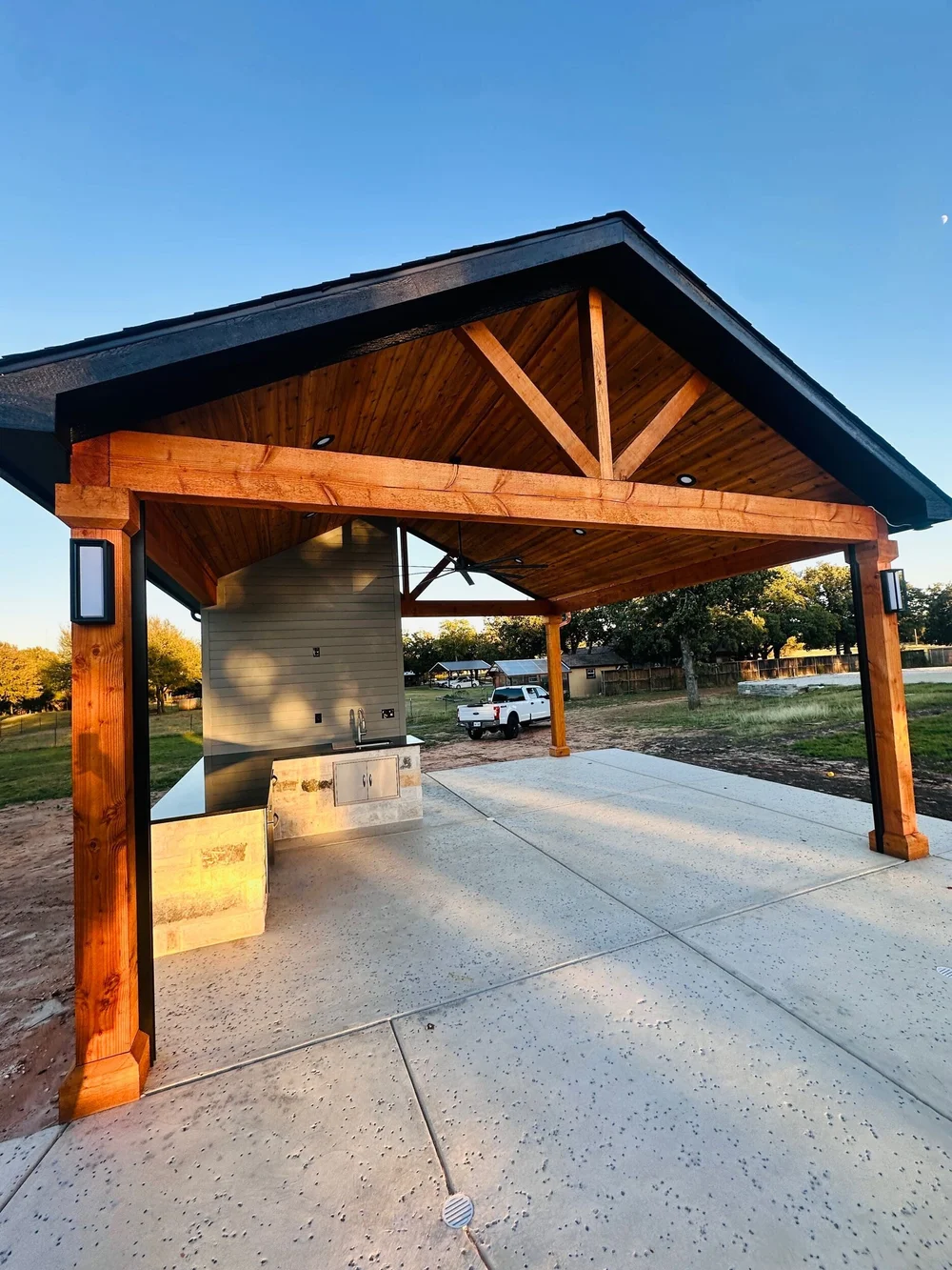 Finished Munday poolside pavilion with gabled wood roof and stone outdoor kitchen in Burleson, Texas