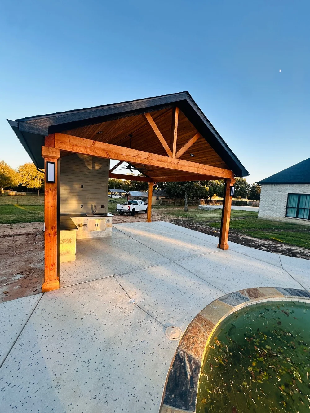 Wide view of the finished Munday gabled pavilion, patio and stone kitchen beside the pool