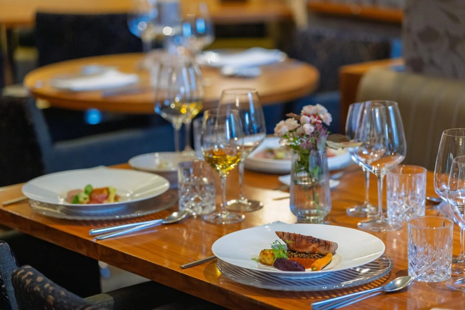 A table set with plated food, wine glasses and flowers at Brioni in Kranj.