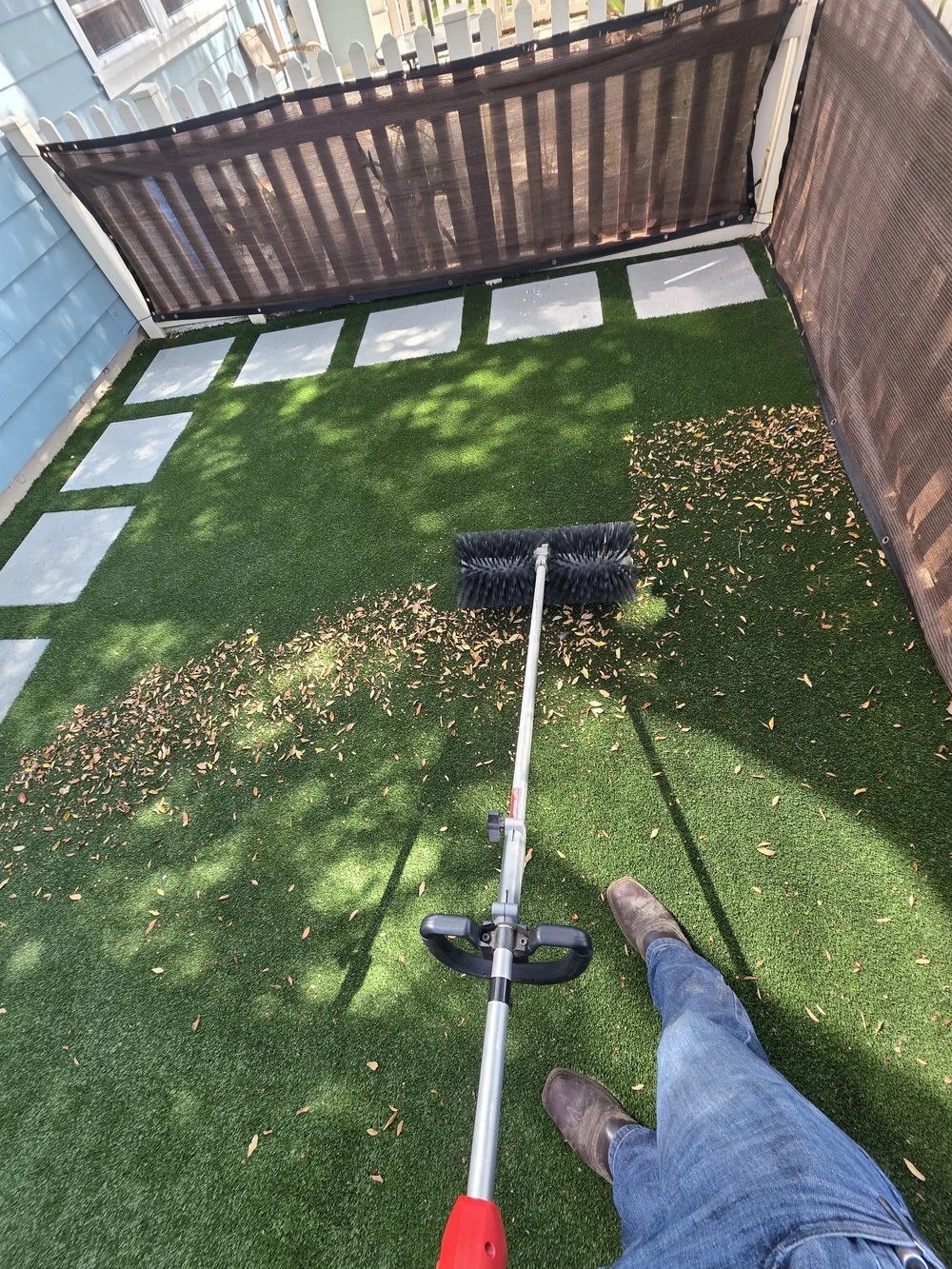 Hydroforce technician power-brooming leaves and debris out of a side-yard artificial turf