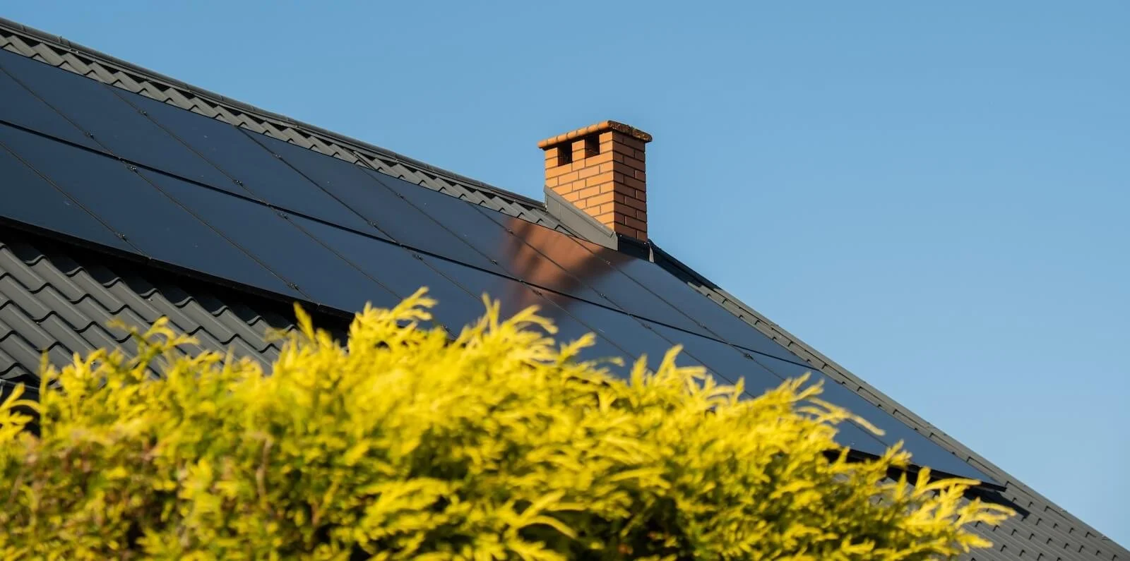 Solar panels fitted to the pitched roof of a house against a clear blue sky.