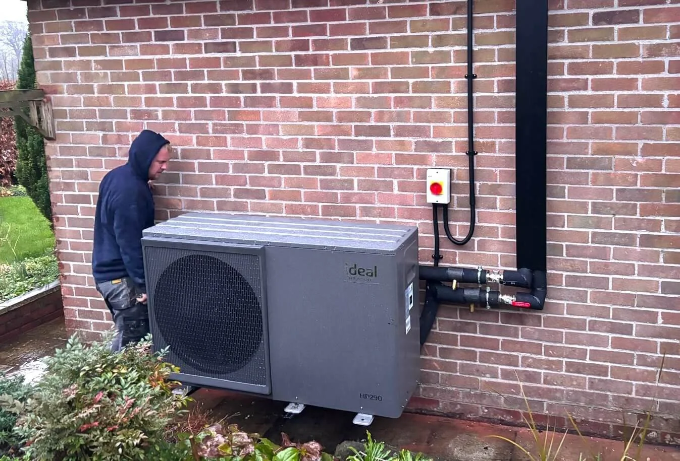 An air source heat pump being installed against the exterior brick wall of a home.