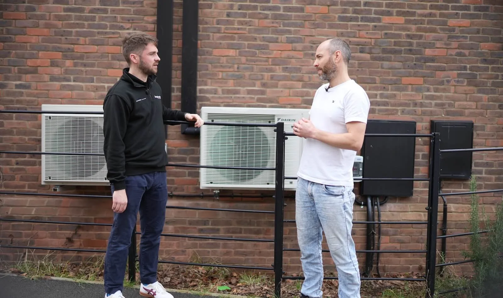 A Simple Solar representative discussing an air source heat pump installation with a homeowner beside the outdoor units