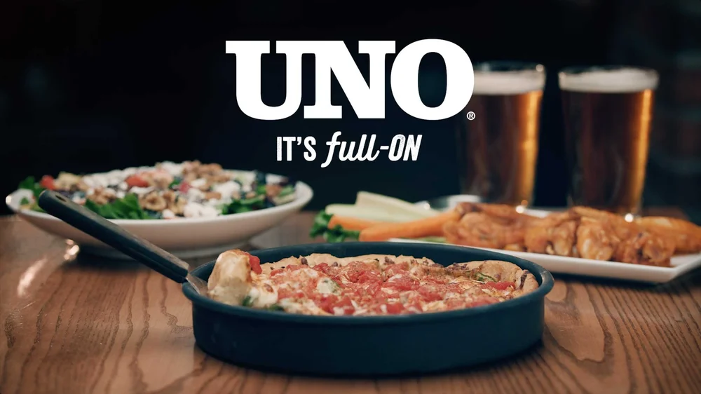 Deep dish pizza, wings, and beer on table in Uno Pizzeria & Grill commercial ad