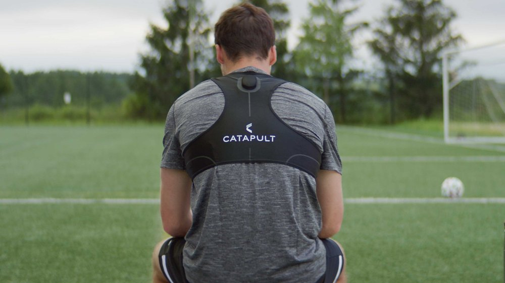 A young athlete sits on a bench facing a soccer field in a Catapult Sports commercial video