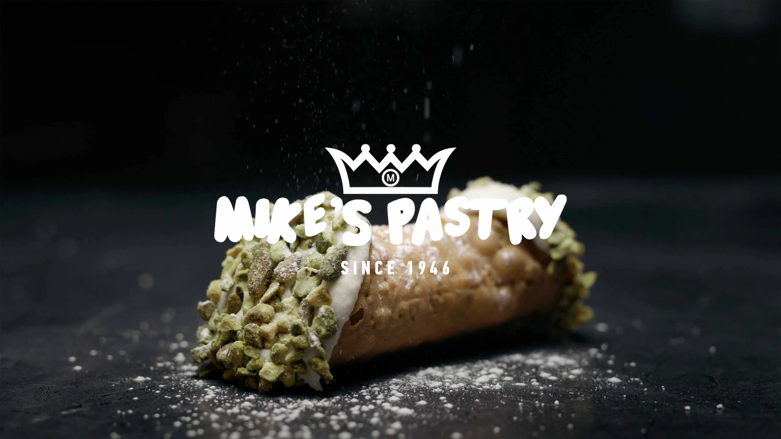 A Mike's Pastry cannoli getting dusted by powdered sugar