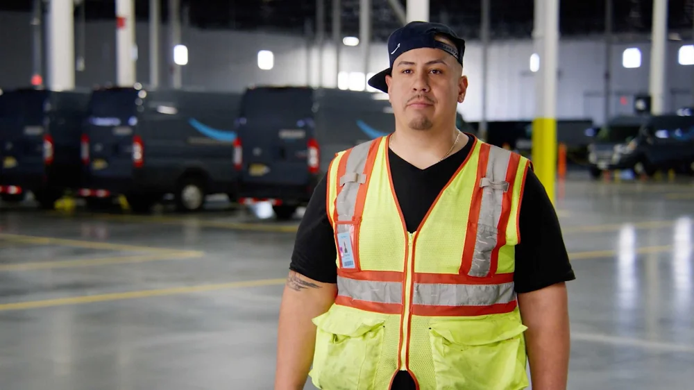 Amazon operations employee Charles Herrera in front of delivery vans at New Jersey fulfillment center for employee story documentary video.