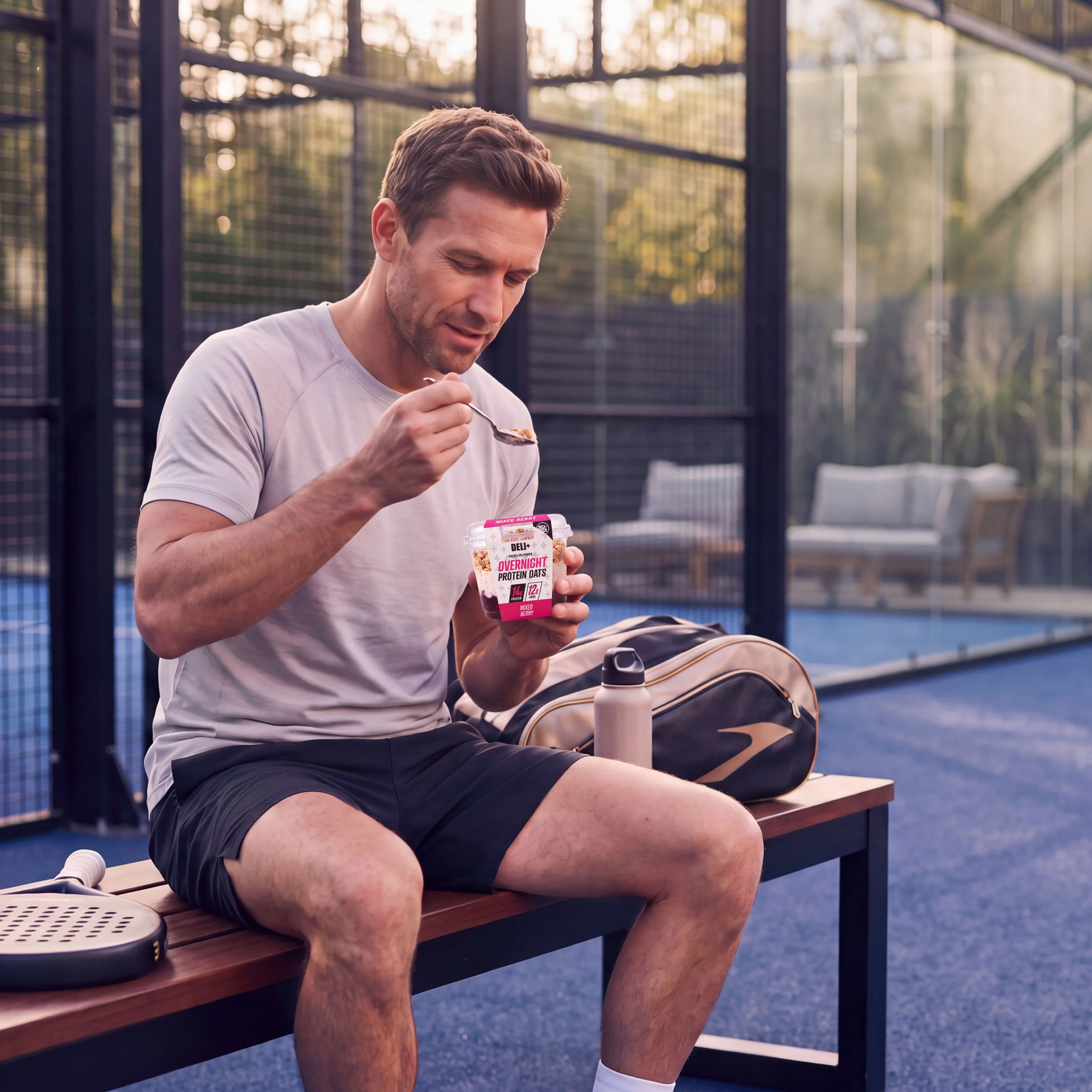 Man eating DELI+ Overnight Protein Oats courtside after a padel session