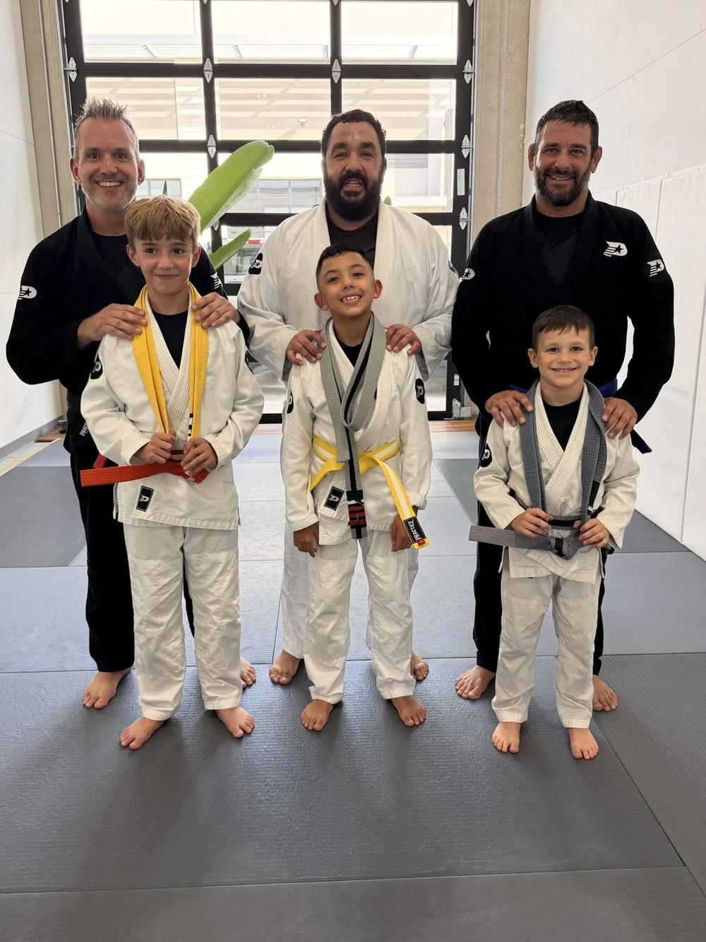 Three young students receiving their new belts alongside their coaches at Practice Jiu Jitsu in Georgetown, TX