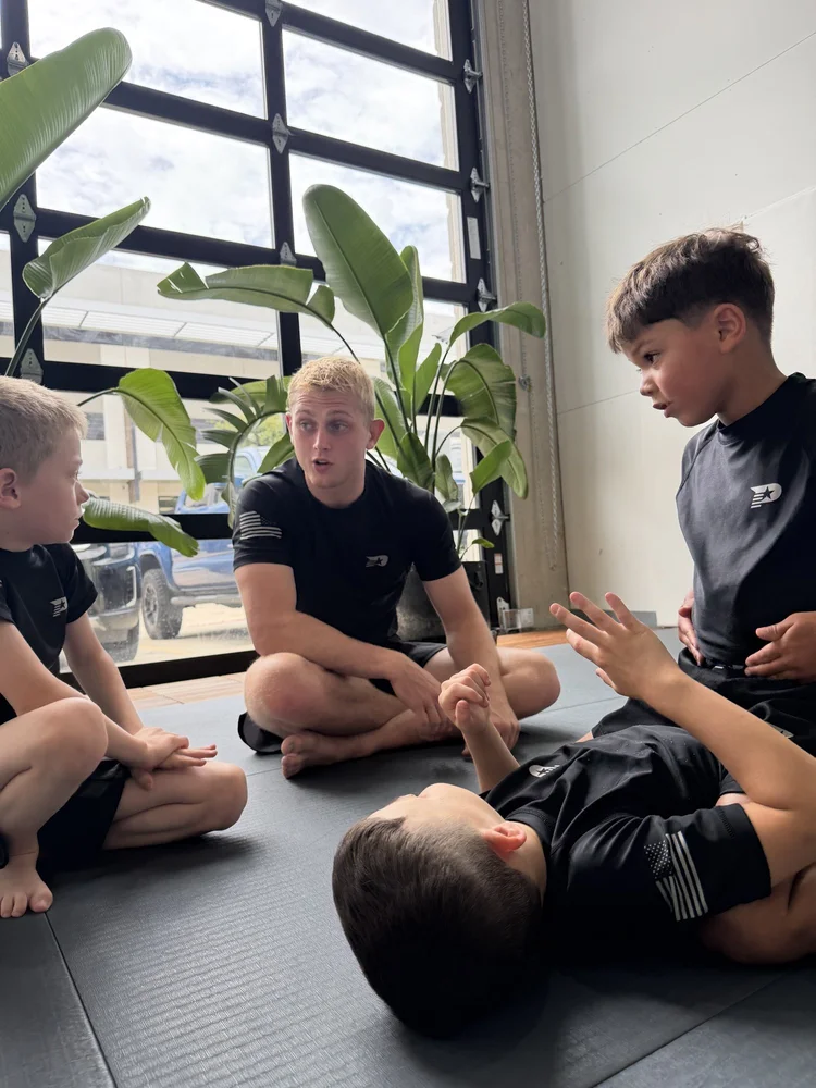 Older kids sitting with their coach during a jiu jitsu class at Practice Jiu Jitsu in Georgetown, TX