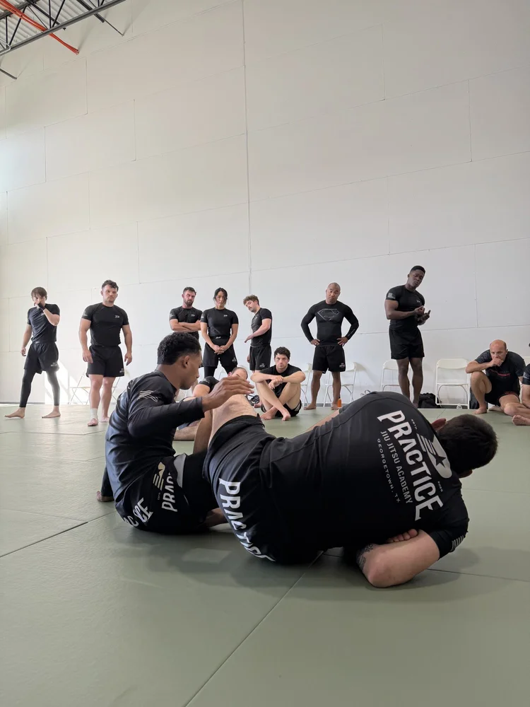 A coach demonstrating a no-gi technique on the mat while students watch during an advanced class at Practice Jiu Jitsu in Georgetown, TX