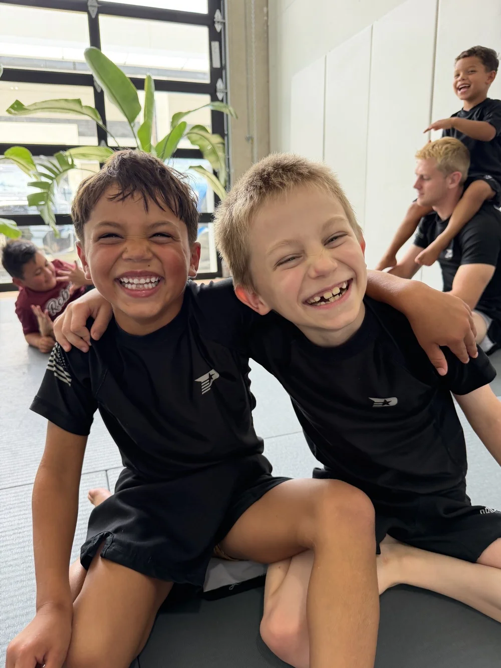Two young boys laughing together with their arms around each other after a kids jiu jitsu class at Practice Jiu Jitsu in Georgetown, TX