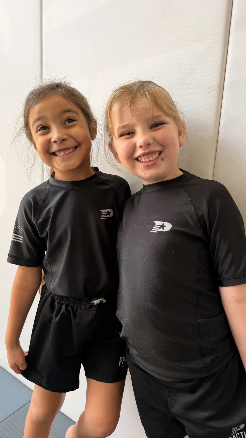 Two girls in Practice Jiu Jitsu shirts smiling together at kids jiu jitsu class in Georgetown, TX