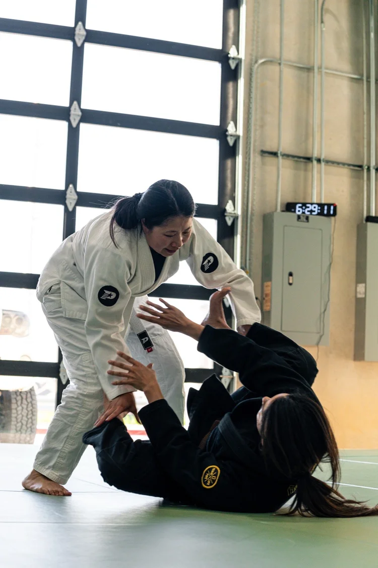 A woman in a white gi and white belt training with a partner during an adult jiu jitsu class at Practice Jiu Jitsu in Georgetown, TX