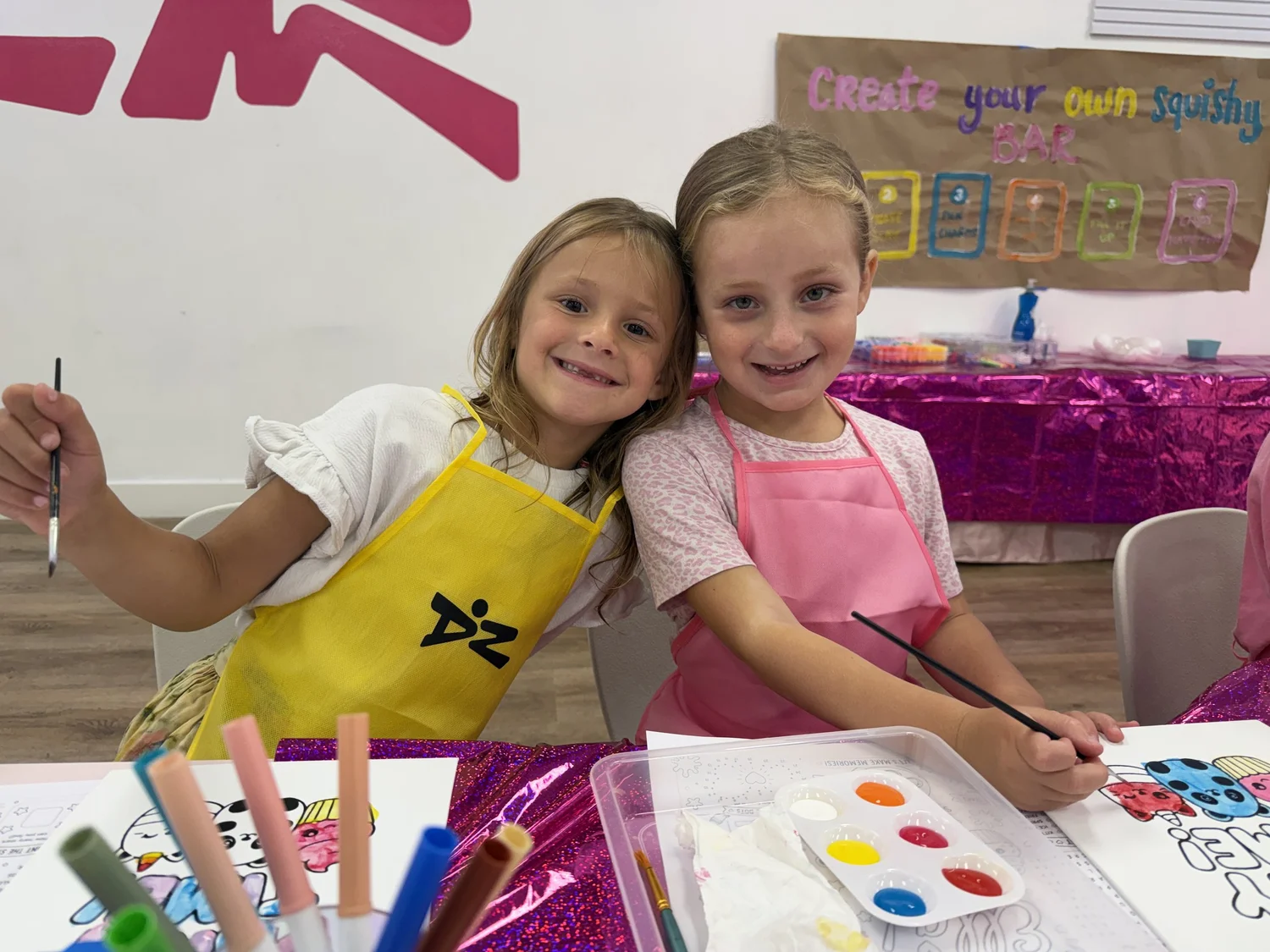 Two smiling campers in Danzone aprons painting at the craft table