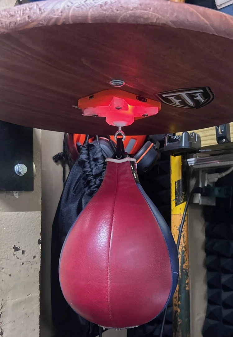 A red speed bag under the glowing orange counter on a wood platform in a garage