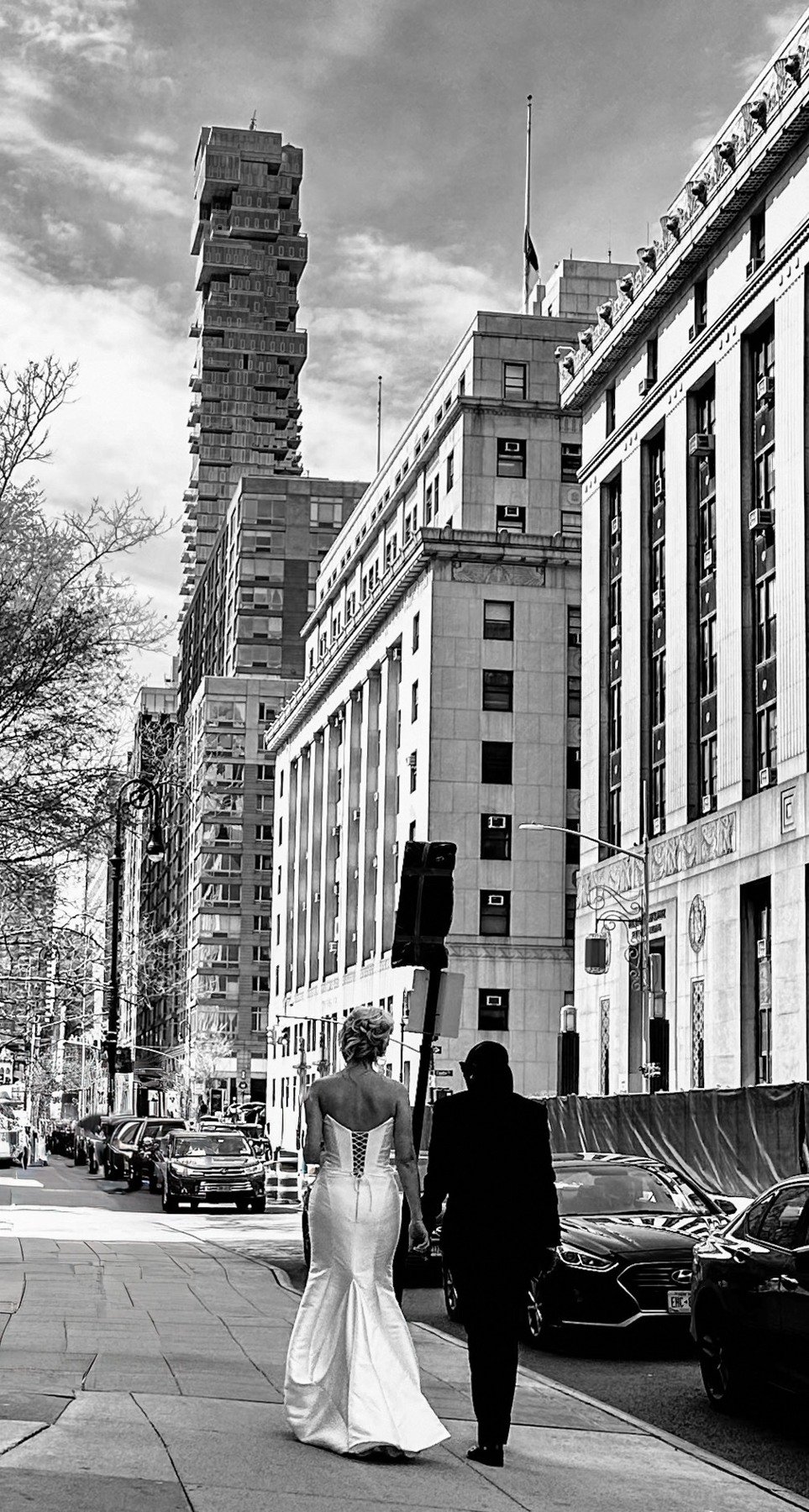Black-and-white street photograph of a couple beneath tall city buildings