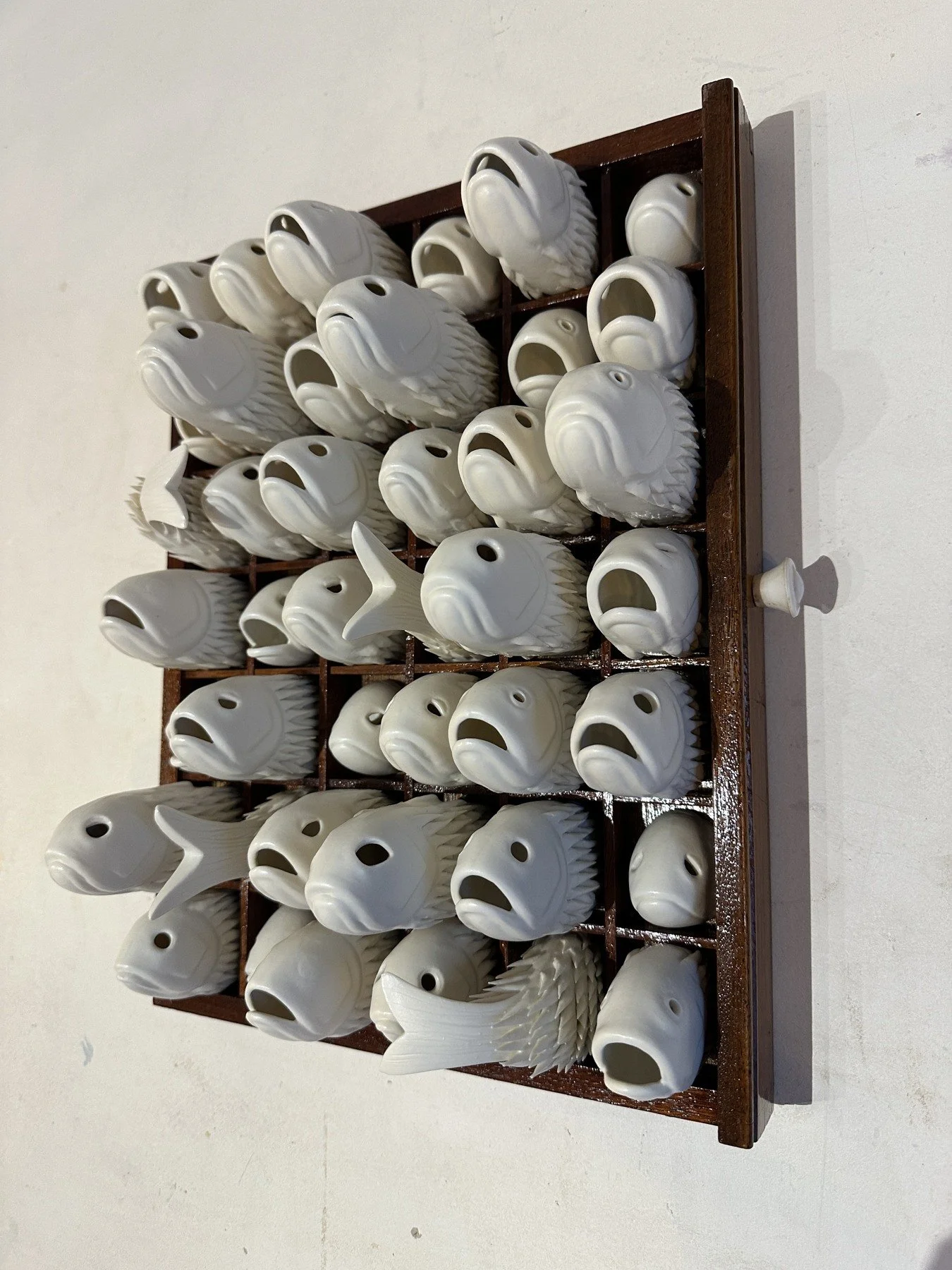 White porcelain fish with open mouths clustered within a dark wooden frame