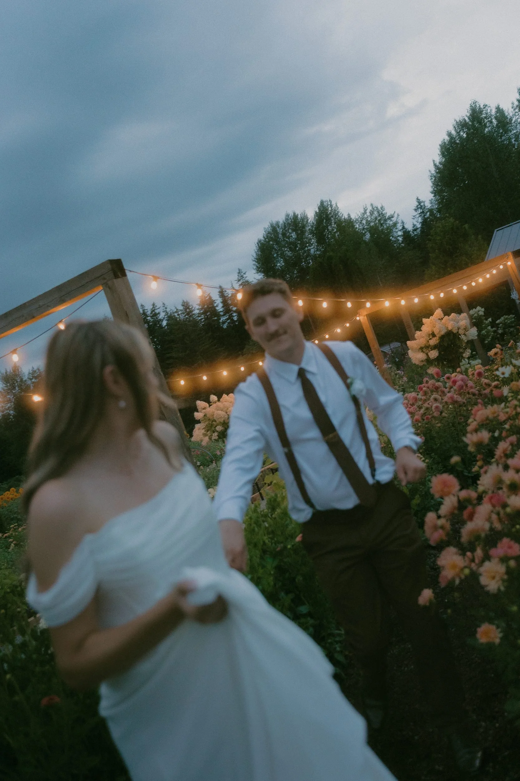 Newlyweds moving through a flower garden beneath string lights