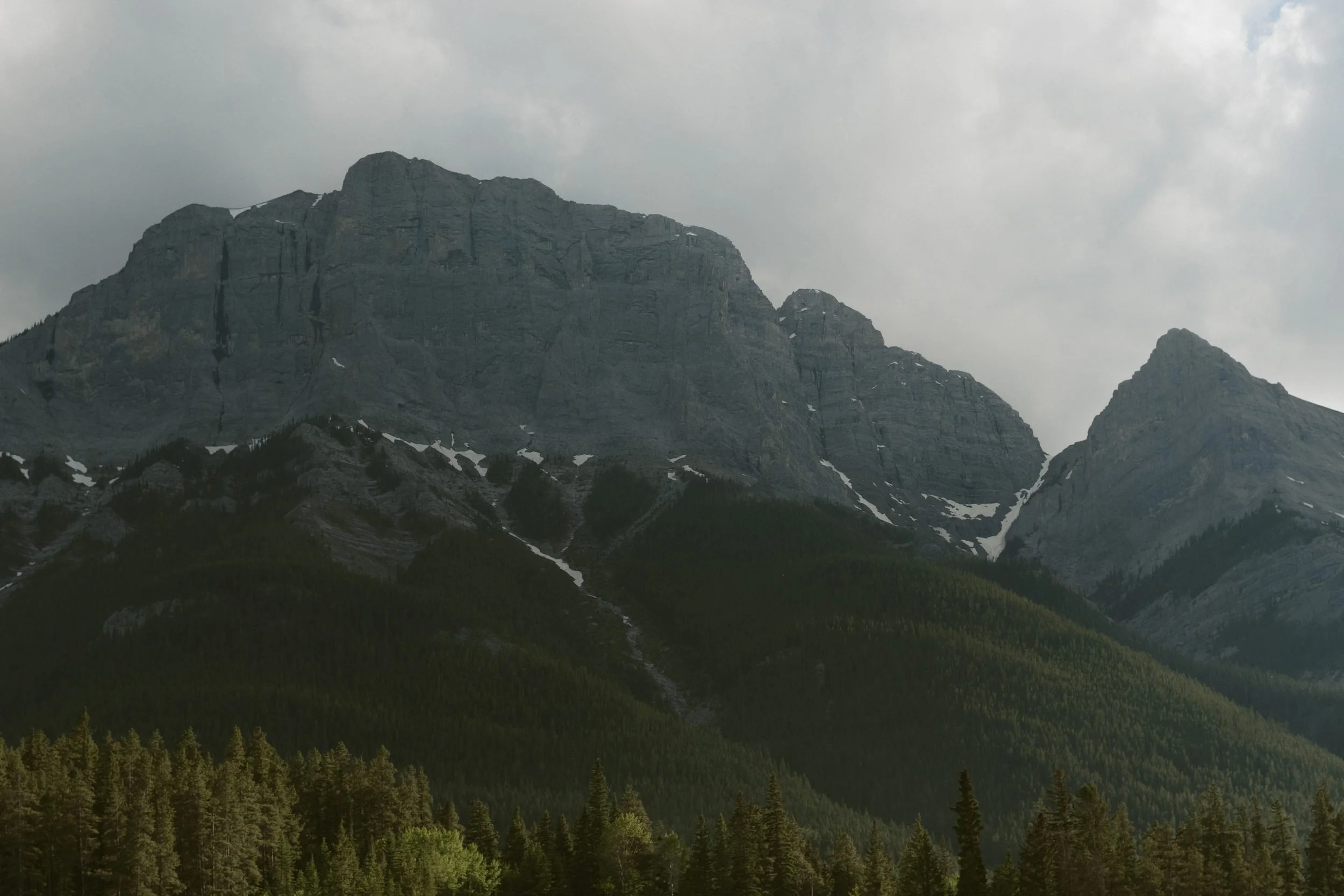 Rocky mountain peaks above forested slopes beneath a cloudy sky