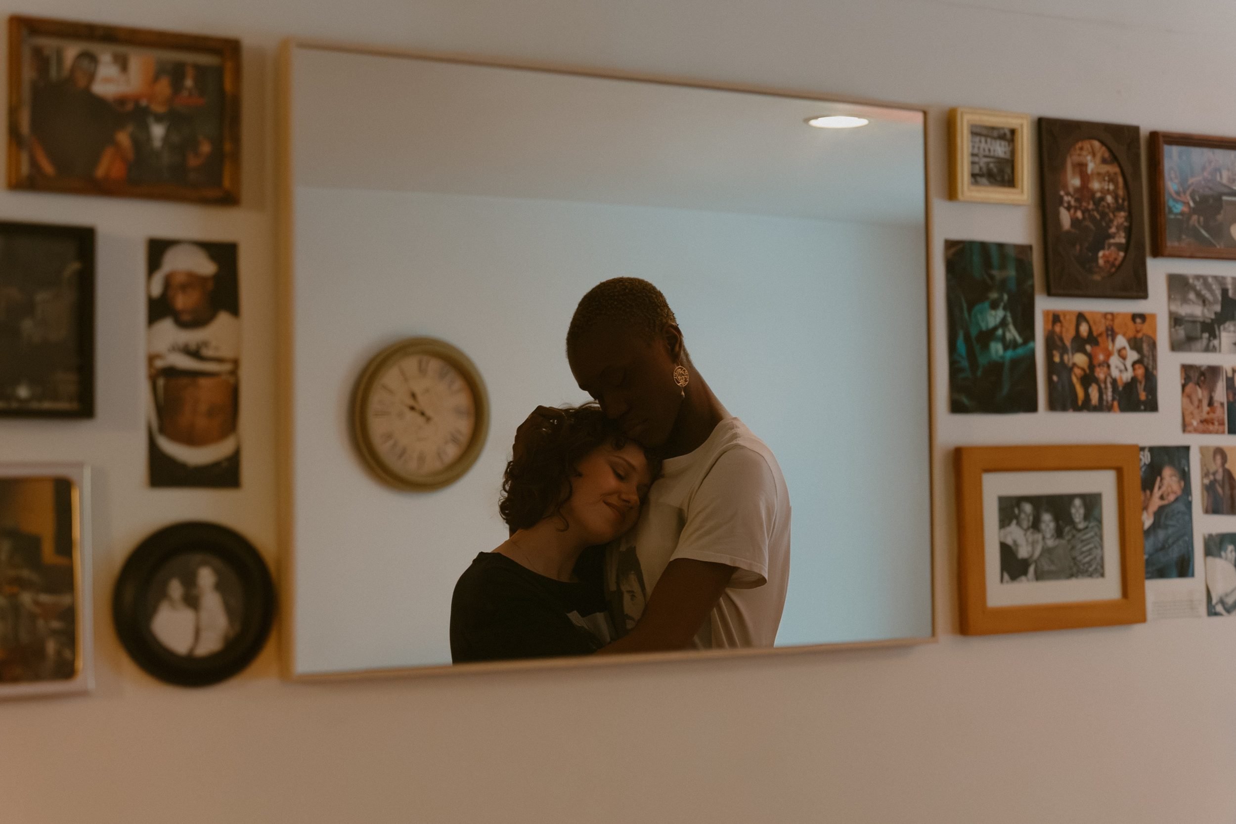 A couple embracing at home, reflected in a mirror surrounded by framed photographs
