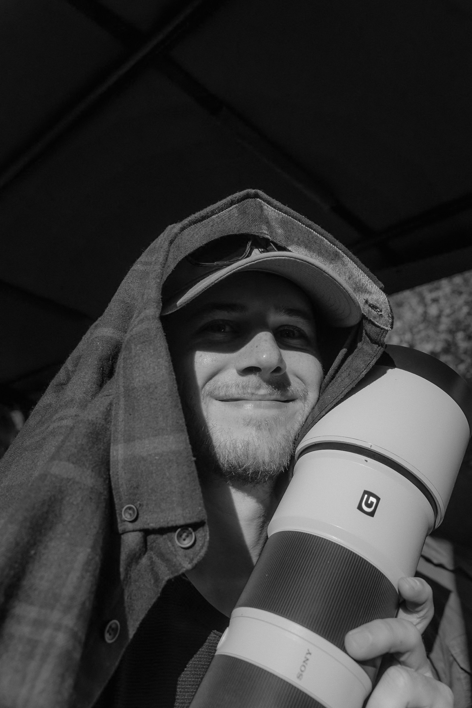 Cam smiling with a telephoto lens tucked beside his face