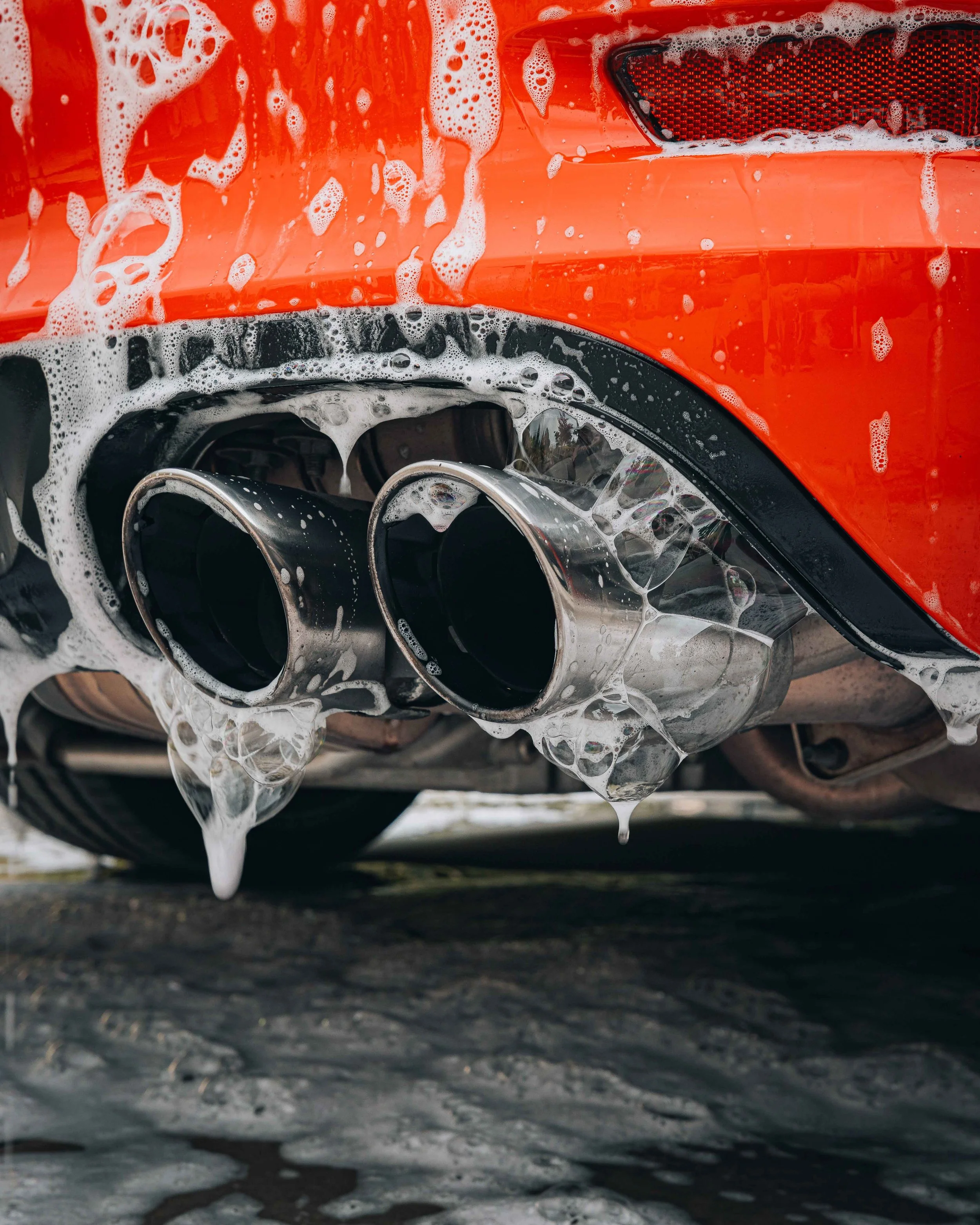 Close-up of polished dual performance exhaust tips on an orange vehicle, highlighting aftermarket exhaust style and finish