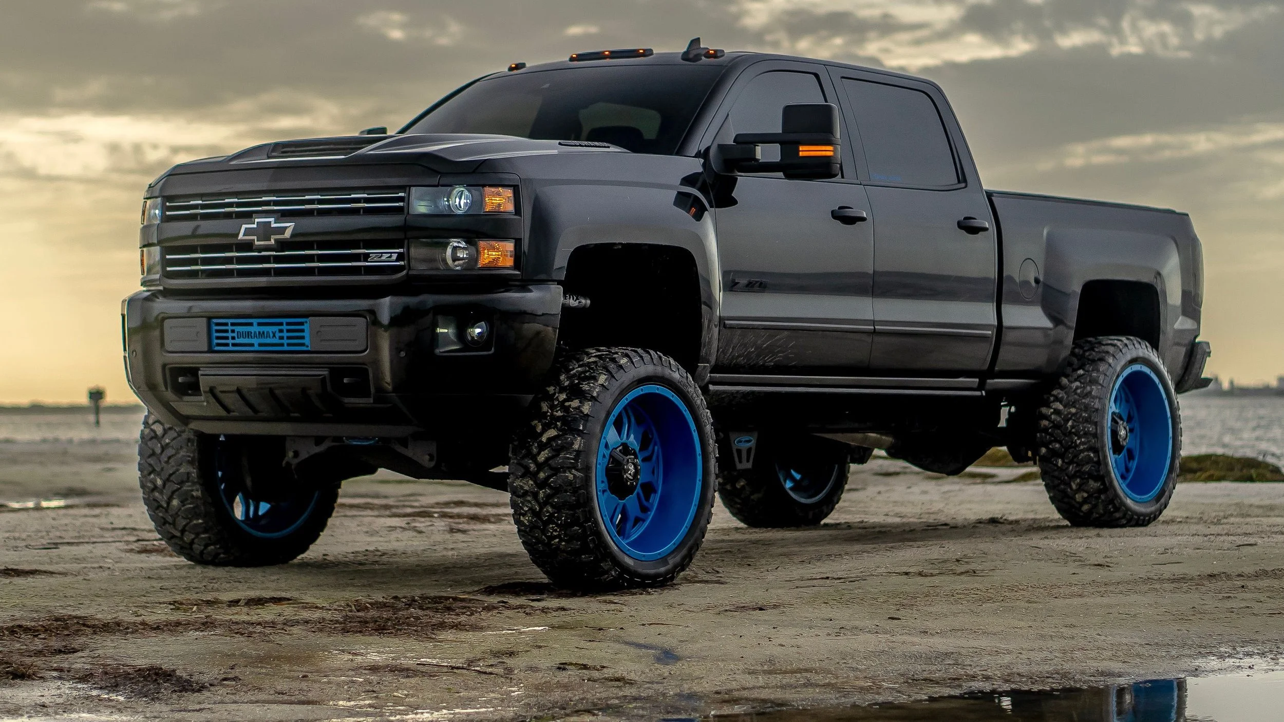 Lifted Chevrolet Silverado Duramax with oversized off-road tires and blue custom truck wheels near Pittsburgh.