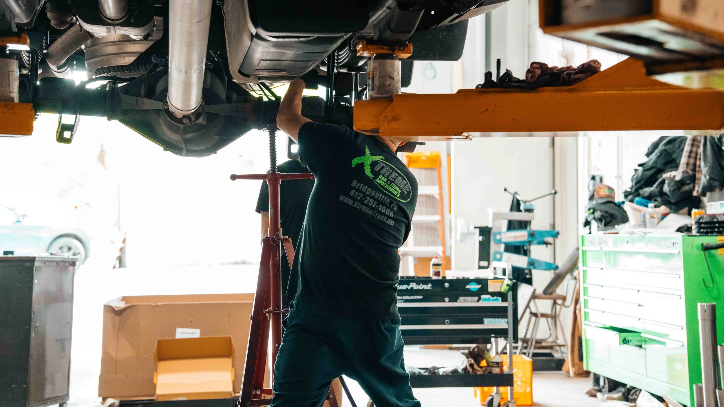 Xtreme Car & Truck technician working under a lifted GMC Sierra during ReadyLIFT 6-inch suspension lift installation in Bridgeville, PA.