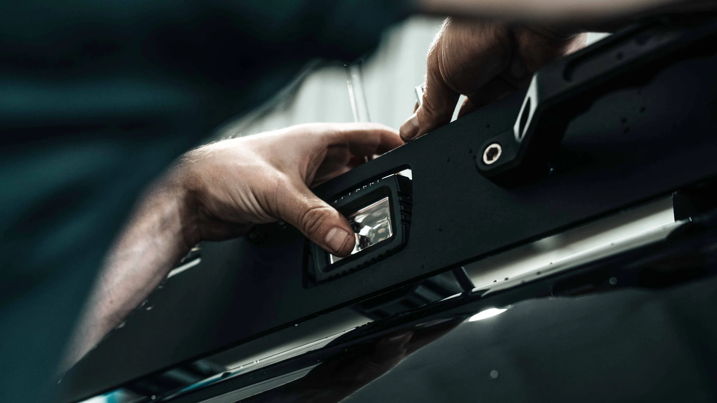 Close view of hands seating a compact LED pod into a cutout in a roof rack wind fairing.