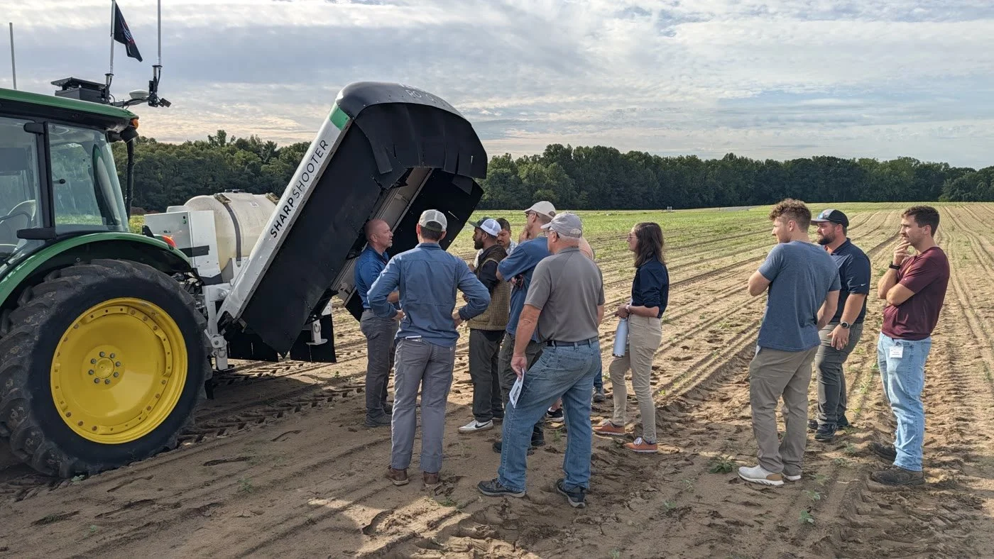 Growers gather beside a raised SharpShooter module for an equipment discussion in the field