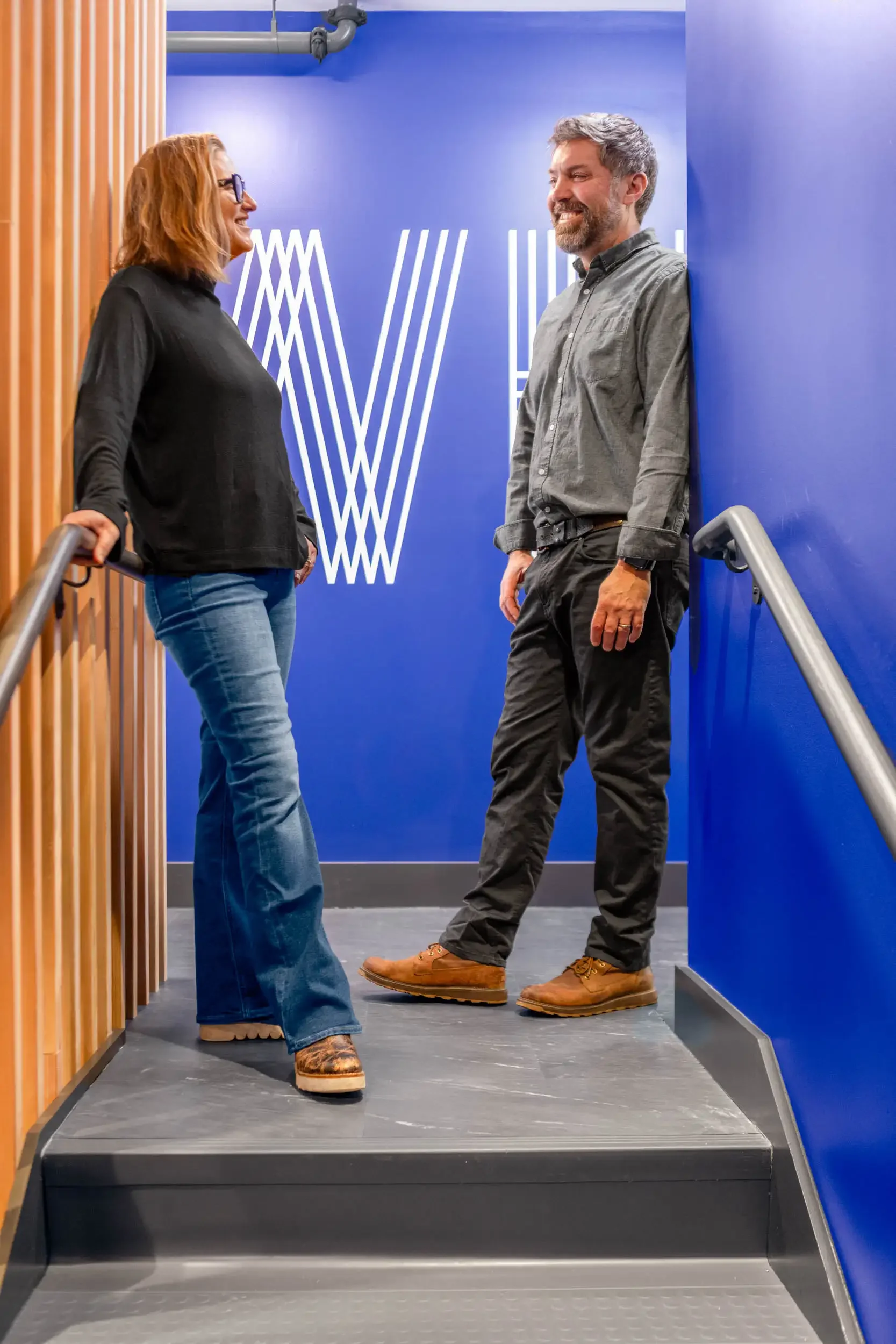 Elisa Winter Holben and Brandon Holben standing on the studio stairs beside the blue Winter Holben wall