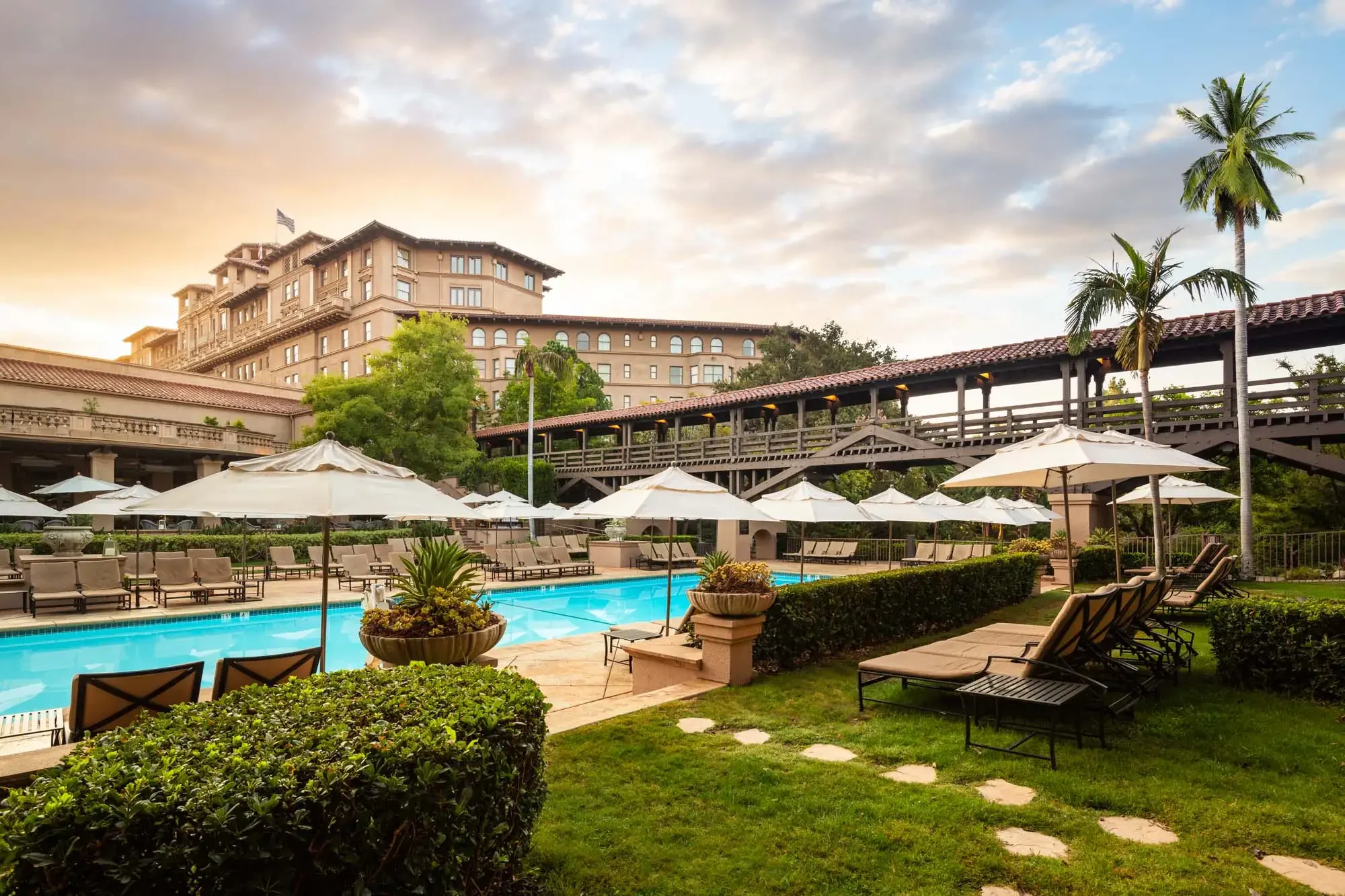 The Langham Huntington hotel overlooking its pool, gardens, and umbrella-shaded loungers in warm evening light