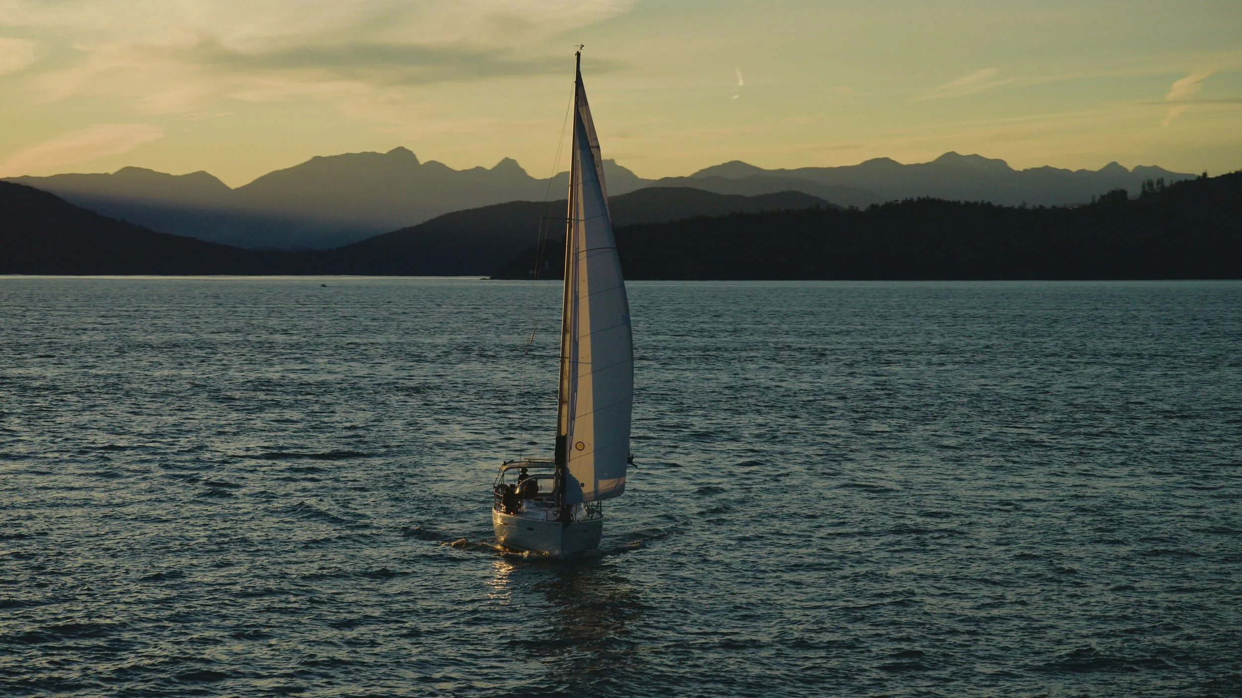 Yacht sailing with mountains at golden hour