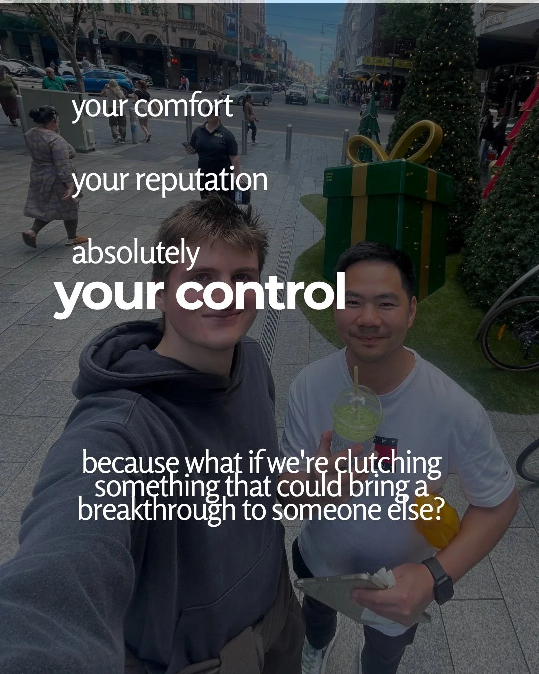 Two young men take a selfie on a city street mall decorated with Christmas trees and a giant gift box. Text: your comfort your reputation absolutely your control because what if we're clutching something that could bring a breakthrough to someone else?