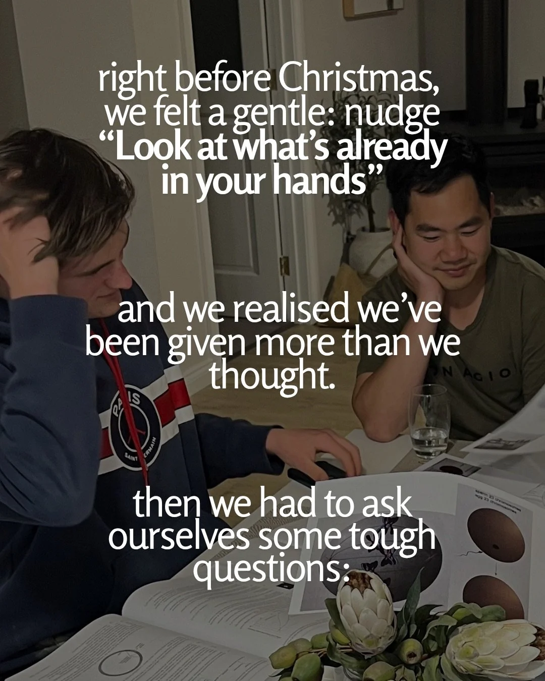 Two young men sit at a dining table covered with open books and papers, one resting his head on his hand, with protea flowers in the foreground. Text: right before Christmas, we felt a gentle: nudge “Look at what’s already in your hands” and we realised we’ve been given more than we thought. then we had to ask ourselves some tough questions: