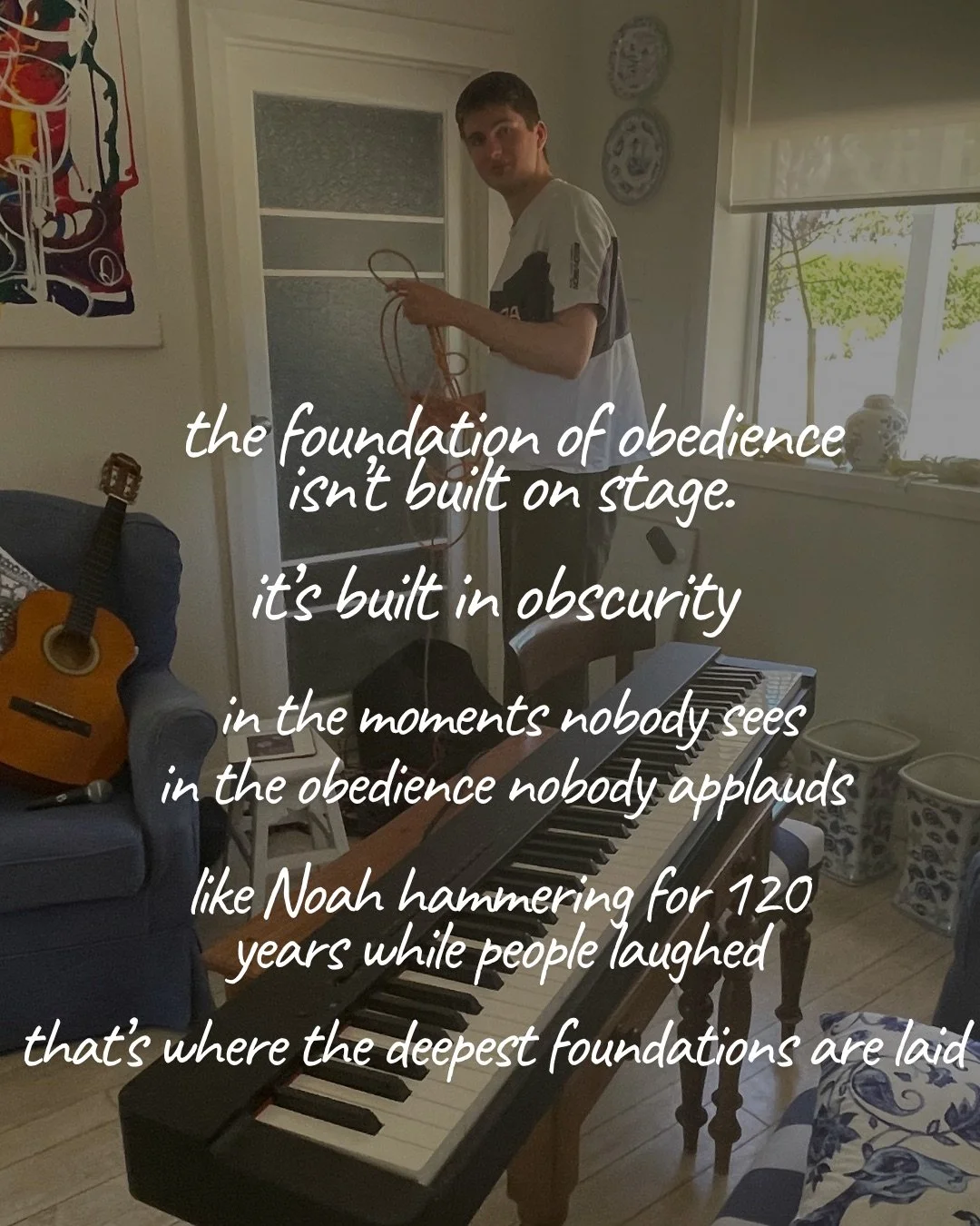 A young man stands holding a cable in a living room with a keyboard in the foreground and a guitar resting on an armchair. Text: the foundation of obedience isn’t built on stage. it’s built in obscurity in the moments nobody sees in the obedience nobody applauds like Noah hammering for 120 years while people laughed that’s where the deepest foundations are laid