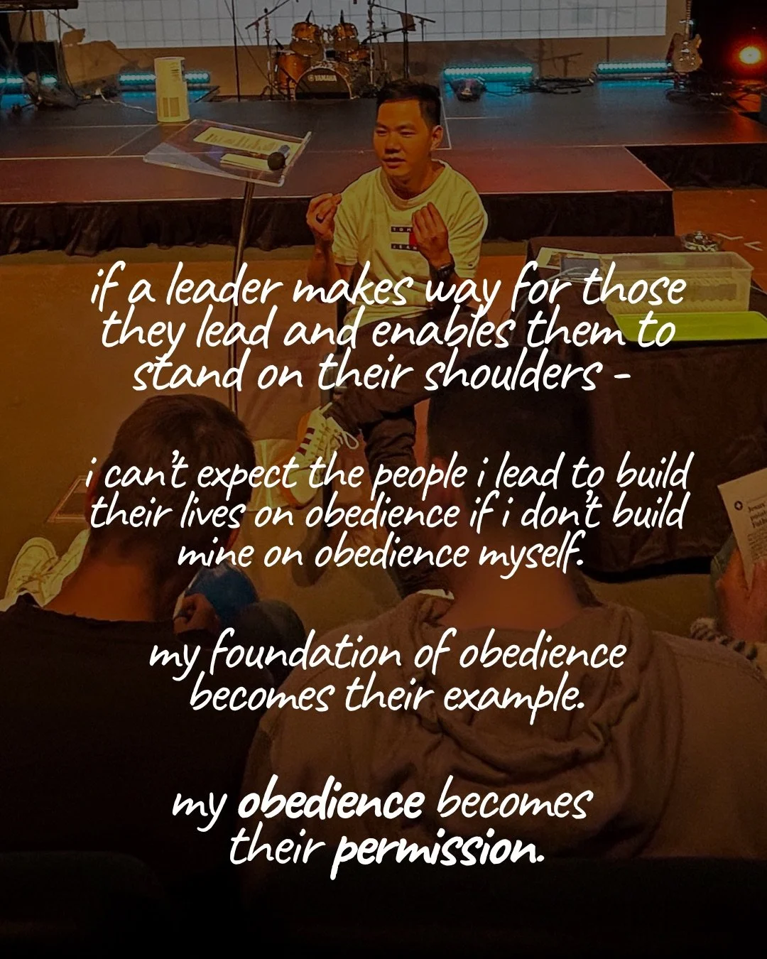 A young man sits speaking to a group seated on the floor in a dim room, with a stage and drum kit behind him. Text: if a leader makes way for those they lead and enables them to stand on their shoulders - i can’t expect the people i lead to build their lives on obedience if i don’t build mine on obedience myself. my foundation of obedience becomes their example. my obedience becomes their permission.