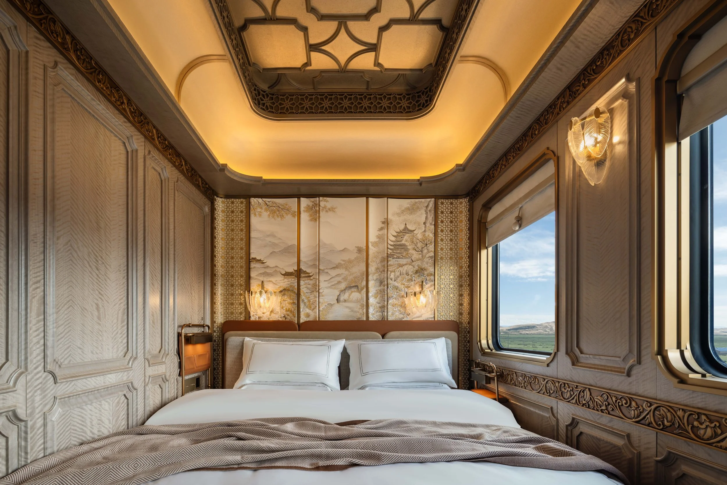 Grand Suite bedroom on the Silk Road Express with a king bed, carved wall panels and a lit coffered ceiling
