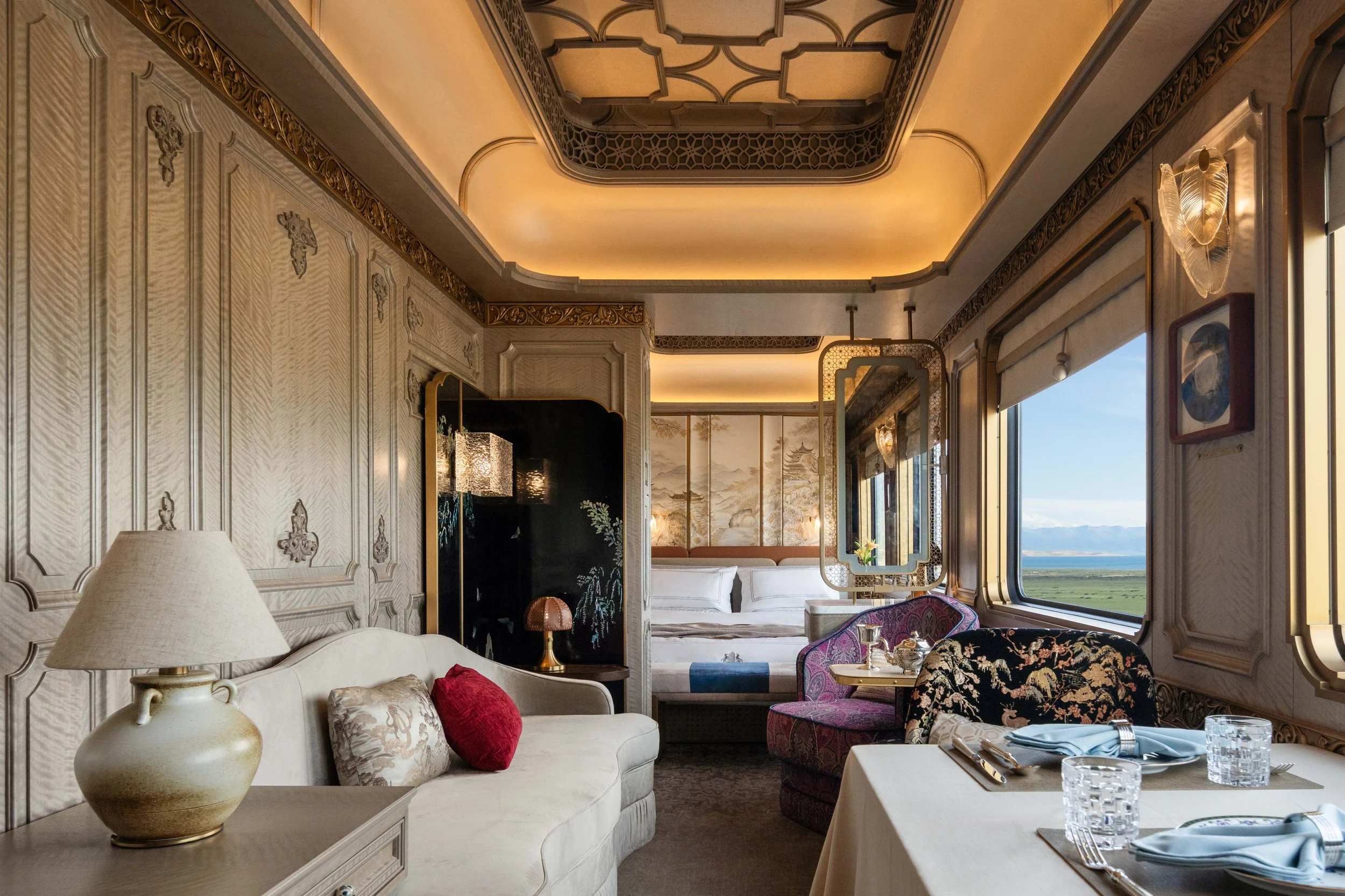 Silk Road Express Grand Suite living room with a sofa, dining table and a window onto a lake and mountains